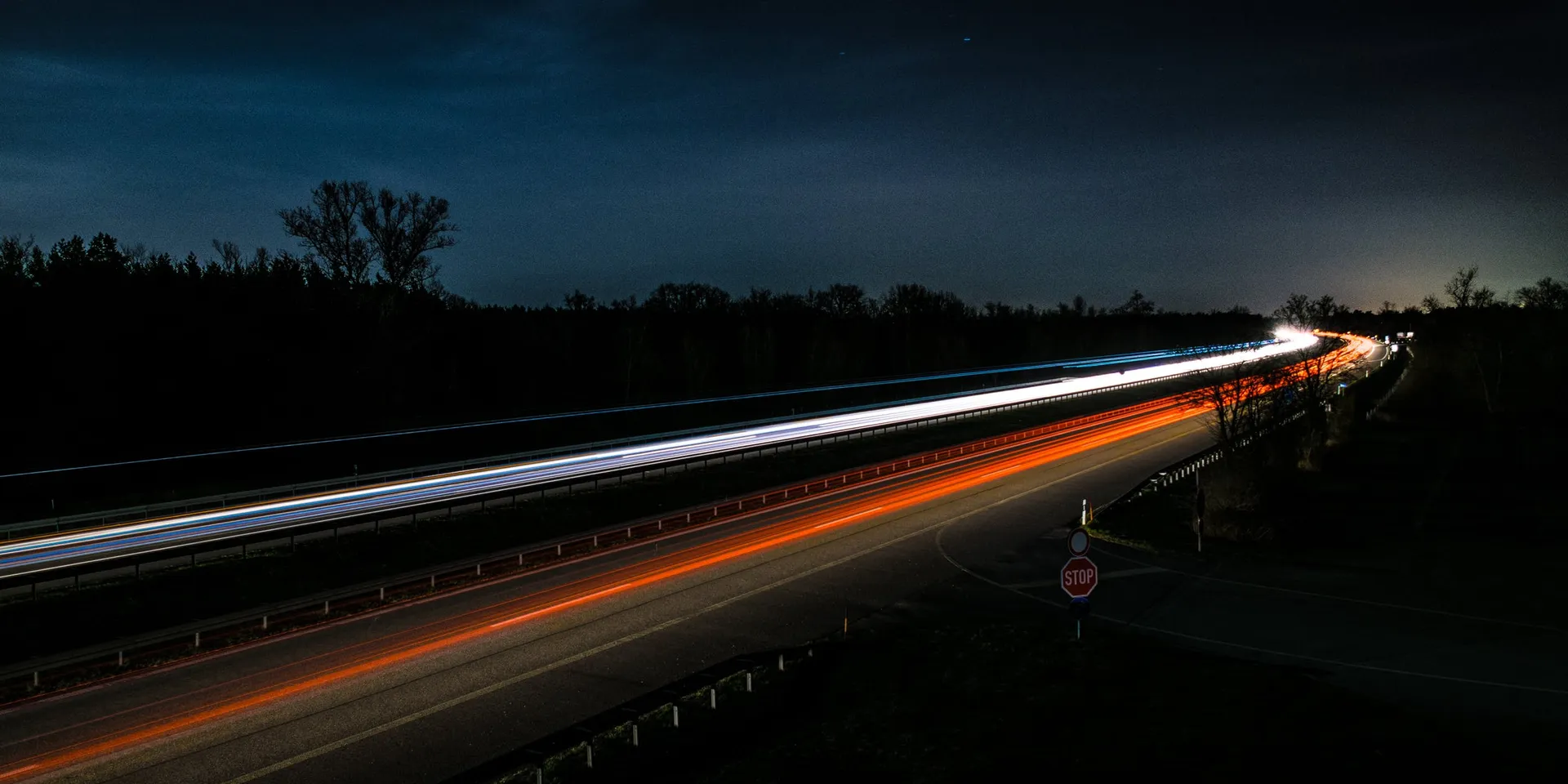 Rodovia à noite em longa exposição, com rastros de luz dos veículos
